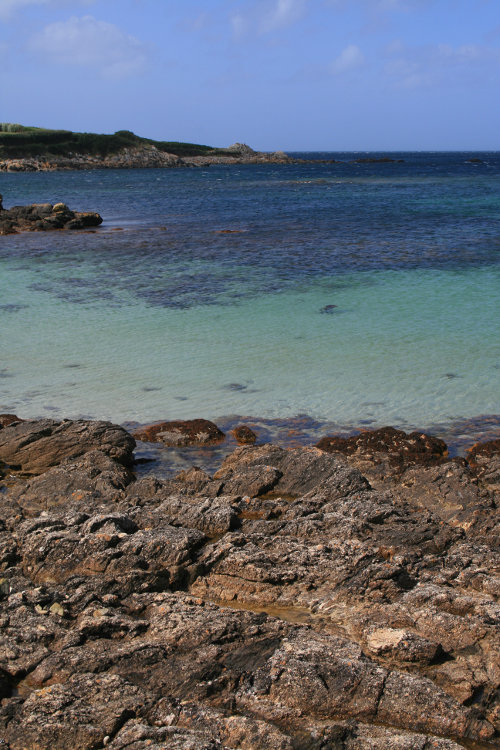 Mer bleutée vue depuis une côte rocheuse par temps calme.