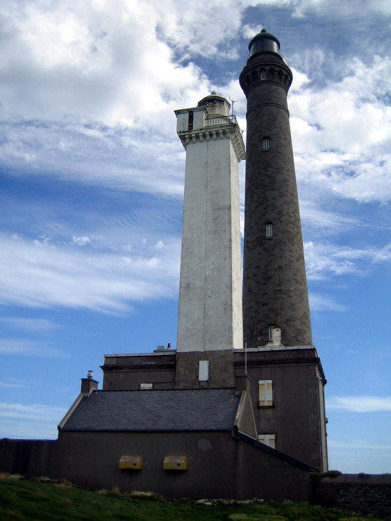 Ancien et nouveau phare de l'île vierge Deux phares de tailles différentes se dressent dans le ciel bleu parsemé de nuages.