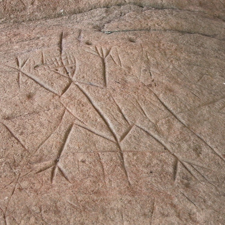 Gravure anthropomorphe sur une pierre rougeâtre.